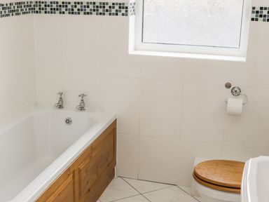A bathroom with a bathtub wooden panel window toilet with wooden seat and tiled walls at McGuire's Cottage Barnatra County Mayo