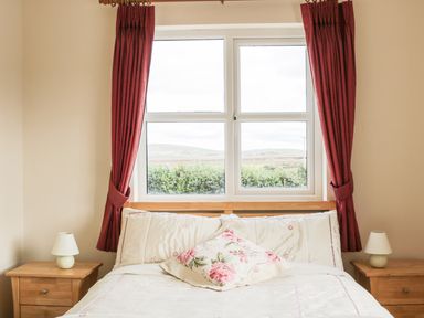 A bedroom with a bed and floral pillow between two wooden nightstands with lamps at McGuire's Cottage Barnatra County Mayo