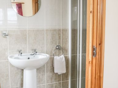 A bathroom sink with a round mirror towel ring with a towel and part of a shower cabin at McGuire's Cottage Barnatra County Mayo
