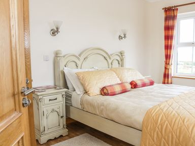 A bedroom with a bed pillows nightstand and window with red and orange curtains at McGuire's Cottage Barnatra County Mayo