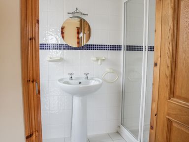 A bathroom with a pedestal sink round mirror and a glass shower door at McGuire's Cottage Barnatra County Mayo