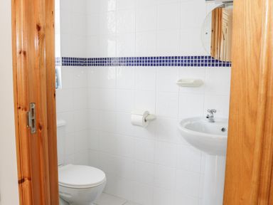 A small bathroom with white tiled walls a toilet a sink and a round mirror at McGuire's Cottage Barnatra County Mayo