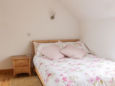A bedroom with a wooden bed and floral bedding next to a wooden nightstand with a light on the wall at McGuire's Cottage in Barnatra County Mayo