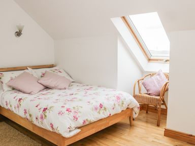A bedroom with a wooden bed with floral bedding and two pillows and a wicker chair with a cushion near a skylight window at McGuire's Cottage Barnatra County Mayo