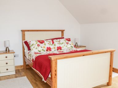 A bedroom with a wooden bed with floral bedding and two bedside tables with lamps at McGuire's Cottage Barnatra County Mayo