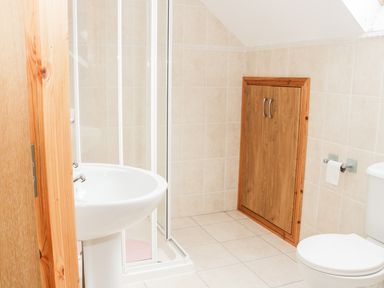 A bathroom with a sink shower cabin toilet wooden storage cupboard and tiled walls at McGuire's Cottage in Barnatra County Mayo