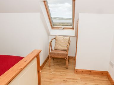 A corner of a room with a wicker chair under a skylight window and part of a bed frame at McGuire's Cottage Barnatra County Mayo