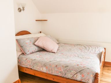 A bedroom with a wooden bed frame a bed with floral bedding and pillows a wall lamp and a wooden shelf at McGuire's Cottage Barnatra County Mayo