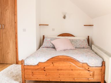 A bedroom with a wooden bed with patterned bedding and a pink pillow a white rug wooden wardrobe and a radiator at McGuire's Cottage Barnatra County Mayo