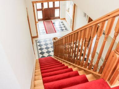 A staircase with a red carpet leading down to an entrance area with a tiled floor and a wooden door at McGuire's Cottage Barnatra County Mayo