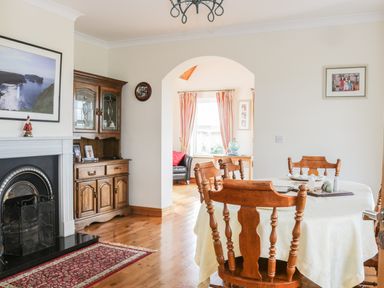A dining room with a wooden table and chairs near a fireplace and a wooden cabinet at McGuire's Cottage Barnatra County Mayo