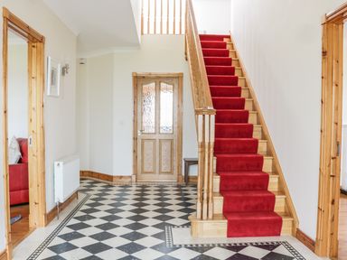 An entryway with black and white checkered floor a wooden staircase with a red runner and wooden door at McGuire's Cottage Barnatra County Mayo