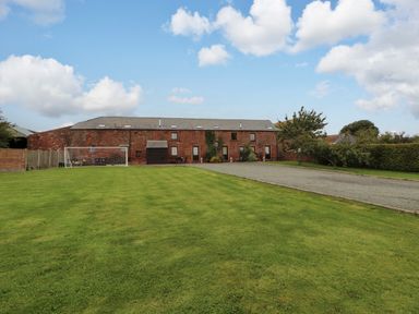An outdoor view of a barn with lawn and gravel driveway at Horseshoe Cottage in Bolton Low Houses