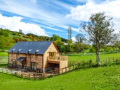 A wooden house with a fenced yard and trees on grassy land at Brynhir Farm in Howey near Llandrindod Wells