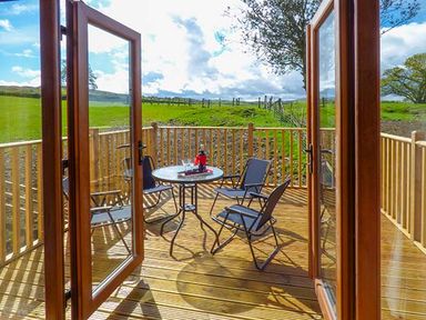 A wooden deck with a round table and four chairs surrounded by a wooden railing at Brynhir Farm in Howey near Llandrindod Wells