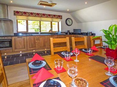 A kitchen with wooden cabinets a dining table set with plates glasses and red napkins and a plant at Brynhir Farm in Howey near Llandrindod Wells