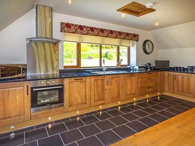 A kitchen with wooden cabinets black countertop stainless steel oven and hood along with a window and clock at Brynhir Farm in Howey near Llandrindod Wells