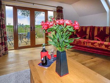 A living room with a wooden table holding flowers and a bottle with glasses by glass doors opening to a balcony at Brynhir Farm in Howey near Llandrindod Wells
