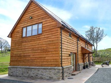 A wooden barn style house with a stone base and gravel driveway outside at Brynhir Farm Howey near Llandrindod Wells