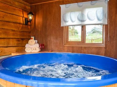 An indoor hot tub with bubbling water near a window and wooden walls with towels and glasses on a shelf at Brynhir Farm in Howey near Llandrindod Wells