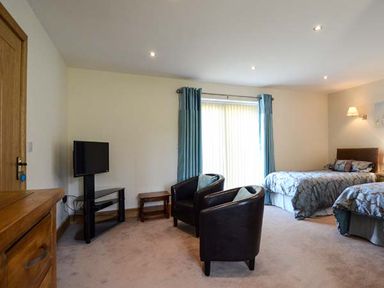 A bedroom with two beds two black chairs a television on a stand and blue curtains at Brynhir Farm in Howey near Llandrindod Wells