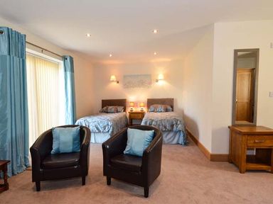 A bedroom with two single beds a wooden nightstand two black armchairs with blue cushions and blue curtains at Brynhir Farm in Howey near Llandrindod Wells