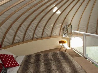 A yurt bedroom with a bed a fur blanket a red pillow a yellow stool and a mirror at Secret Island Yurt in Beckford near Tewkesbury