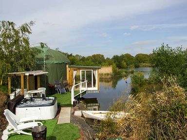 A green yurt with outdoor chairs table and a hot tub next to a river at Secret Island Yurt Beckford near Tewkesbury