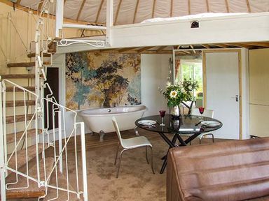 An interior room with a spiral staircase a round glass table with chairs and a freestanding bathtub with a floral wall behind at Secret Island Yurt Beckford near Tewkesbury