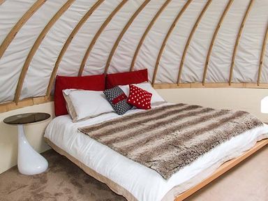 A bedroom with a bed with pillows and a blanket and a side table at Secret Island Yurt Beckford near Tewkesbury