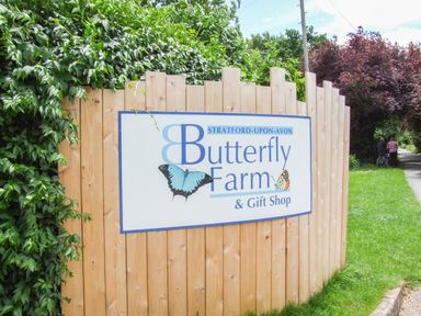A wooden fence with a sign for Stratford-Upon-Avon Butterfly Farm and Gift Shop beside a grassy path