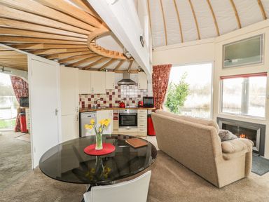 An open plan kitchen and living area with a round glass dining table a beige sofa and a fireplace at Secret Island Yurt Beckford near Tewkesbury