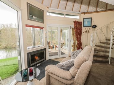A living area with a beige sofa near a fireplace and glass doors with views of a river at Secret Island Yurt in Beckford near Tewkesbury