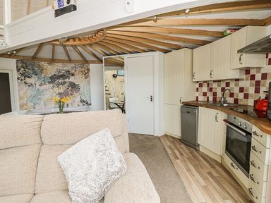 A kitchen with cream cabinets and patterned backsplash next to a beige sofa with cushions at Secret Island Yurt in Beckford near Tewkesbury
