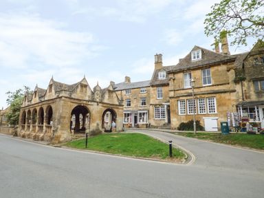 A stone market hall structure with arches next to historic stone buildings on a street with green grass at Secret Island Yurt in Beckford near Tewkesbury
