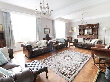 A living room with four leather sofas a patterned rug a wooden cabinet and chandeliers at Bryn Derwen in Bethesda near Caernarfon