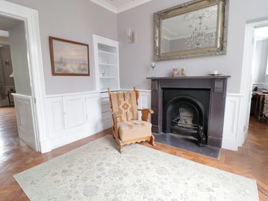 A room with a patterned armchair a fireplace with a mirror above and wall art at Bryn Derwen in Bethesda near Caernarfon