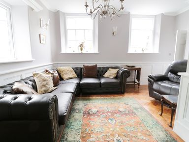 A living room with black leather sofas a patterned rug and a wooden side table at Bryn Derwen in Bethesda near Caernarfon