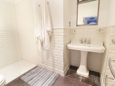 A bathroom with a pedestal sink mirror towels and a shower area at Bryn Derwen Bethesda near Caernarfon