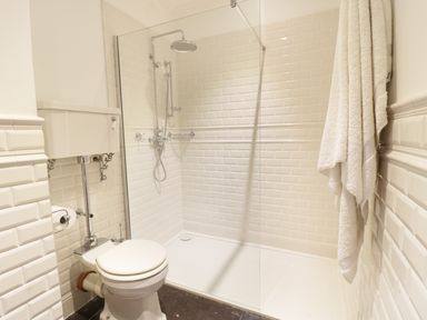 A bathroom with a toilet shower area white tiles and towels hanging at Bryn Derwen in Bethesda near Caernarfon
