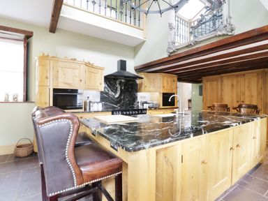 A kitchen with a large marble island countertop wooden cabinets leather chairs and exposed wooden beams at Bryn Derwen in Bethesda near Caernarfon