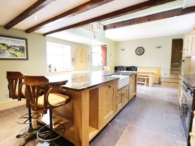 A kitchen with a wooden island and two bar stools under wooden ceiling beams at Bryn Derwen in Bethesda near Caernarfon