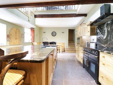 A kitchen with wooden cabinets a black stove a marble countertop island with a chair and stairs at Bryn Derwen in Bethesda near Caernarfon