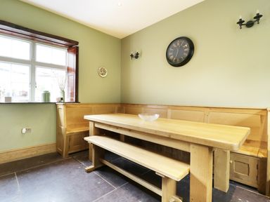 A dining area with wooden bench seating and a table under a wall clock at Bryn Derwen Bethesda near Caernarfon