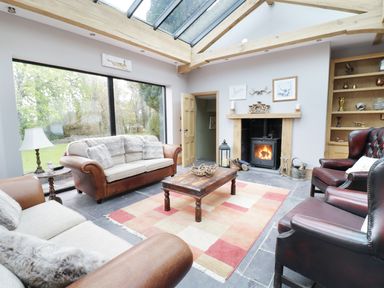A living room with sofas chairs a coffee table a fireplace and large windows at Bryn Derwen Bethesda near Caernarfon