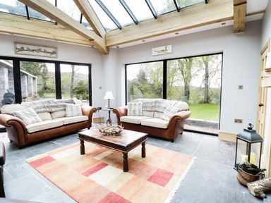 A living room with two sofas a wooden coffee table a floor lamp and large windows at Bryn Derwen Bethesda near Caernarfon