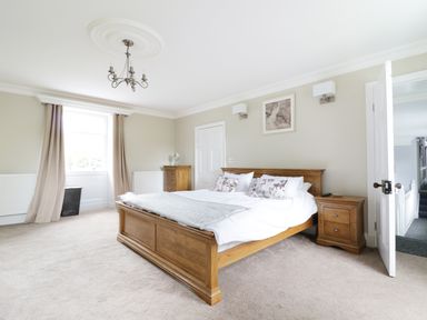 A bedroom with a wooden bed a bedside table a chest of drawers a window with curtains and a chandelier at Bryn Derwen in Bethesda near Caernarfon