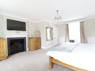A bedroom with a bed wooden dressers a fireplace a wall mounted television and a window with curtains at Bryn Derwen in Bethesda near Caernarfon