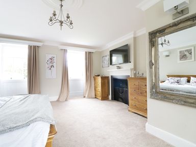 A bedroom with wooden dressers a fireplace a television and a large mirror at Bryn Derwen in Bethesda near Caernarfon