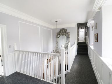 A hallway with white railings a large ornate mirror wall sconces and carpet at Bryn Derwen in Bethesda near Caernarfon